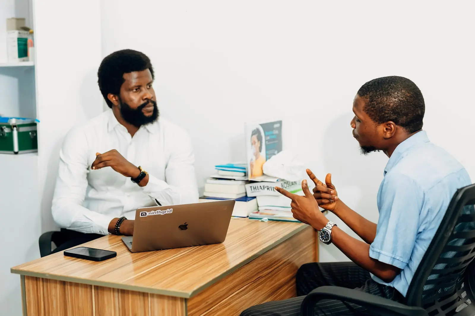 A doctor and a patient talk across a desk in a clinic office.