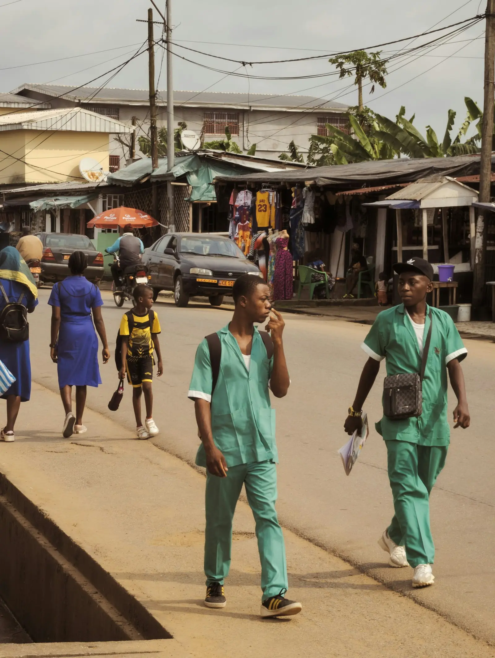 Two health workers in green scrubs walking along a busy street.